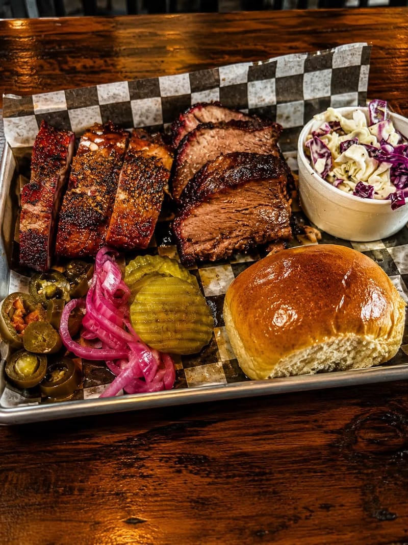 Sliced smoked brisket on a tray with ribs and coleslaw