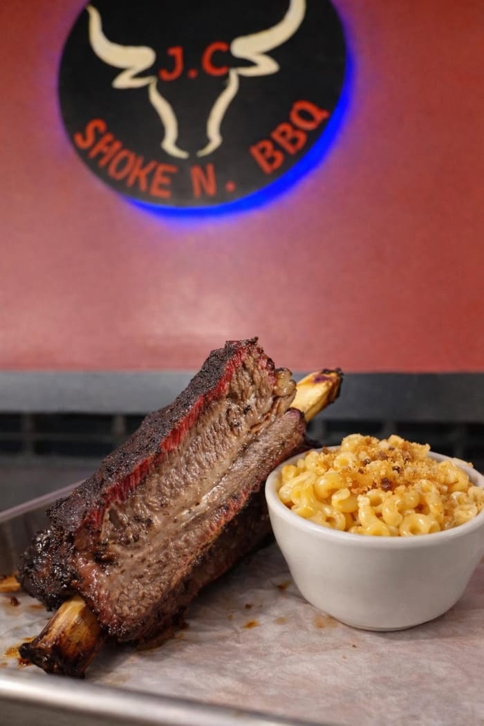 A bowl of baked mac and cheese next to a smoked beef rib