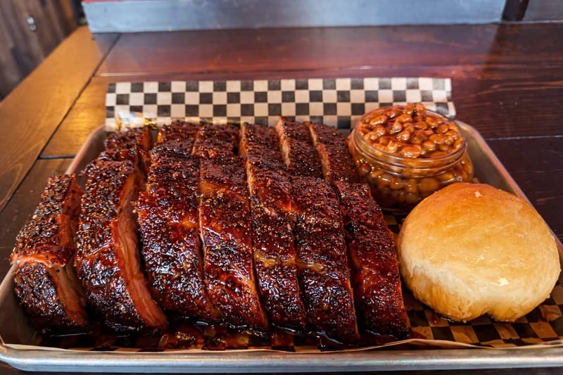 Glazed sliced pork ribs with baked beans and a roll