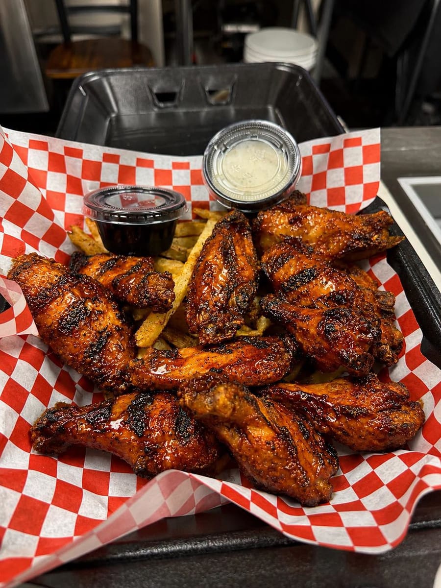A basket of glazed smoked wings with fries and dipping sauces